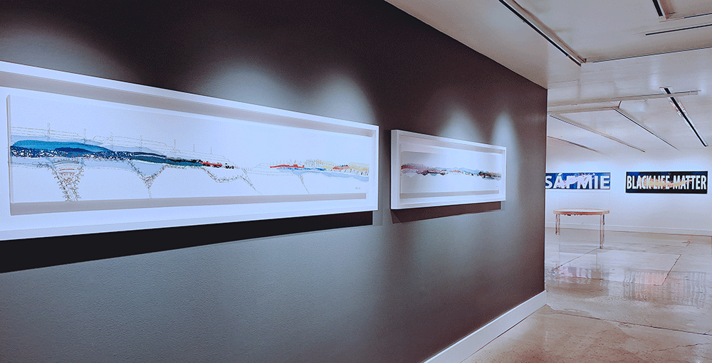 Installation view showing embroidered landscape artwork on dark gallery wall